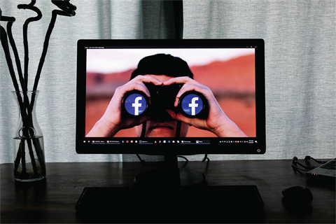 Looking Through Binoculars at the Facebook Logo.